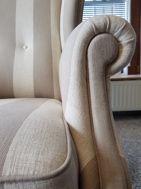 Close-up of a beige and light brown striped upholstered armchair featuring a rolled armrest and cushioned seat.