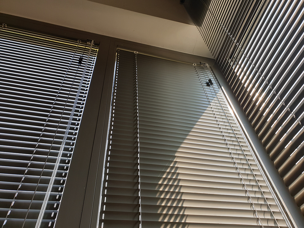 Three large windows with white horizontal blinds partially open, casting shadows on the walls.