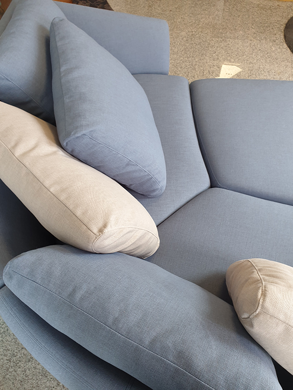 Close-up of a sectional sofa with light blue and beige cushions on a carpeted floor.