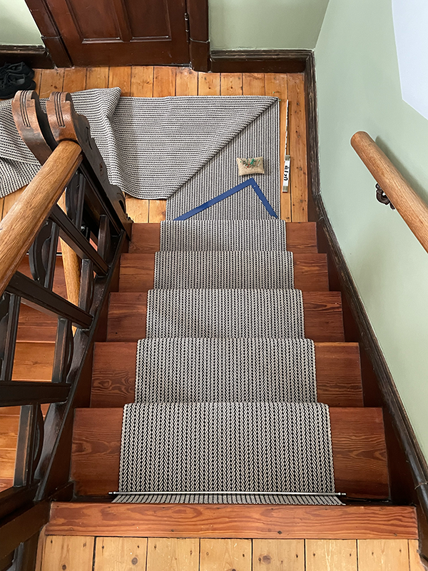 Wooden staircase with a patterned carpet runner installed and folded back on the landing at the top.