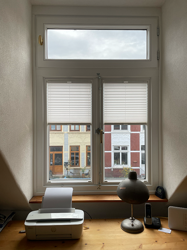 Wooden desk with a printer, a desk lamp, and a cordless phone in front of a window showing residential buildings outside.