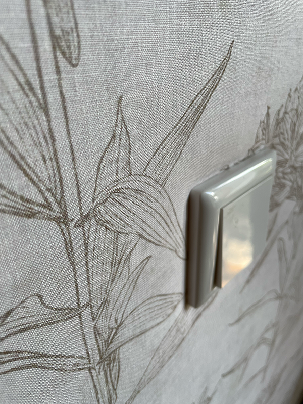 White light switch mounted on wall with beige floral patterned wallpaper.