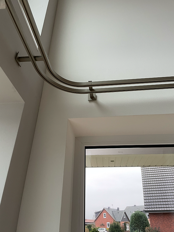 Modern metal curtain rods mounted on a white wall above a window showing houses and trees outside.