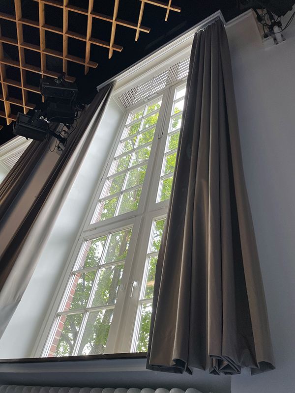 Tall white-framed window partially covered by long gray curtains with green leafy trees visible outside.