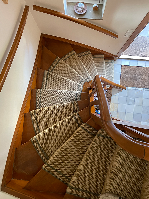 Top-down view of a curved wooden staircase with patterned runners on each step and wooden handrails.